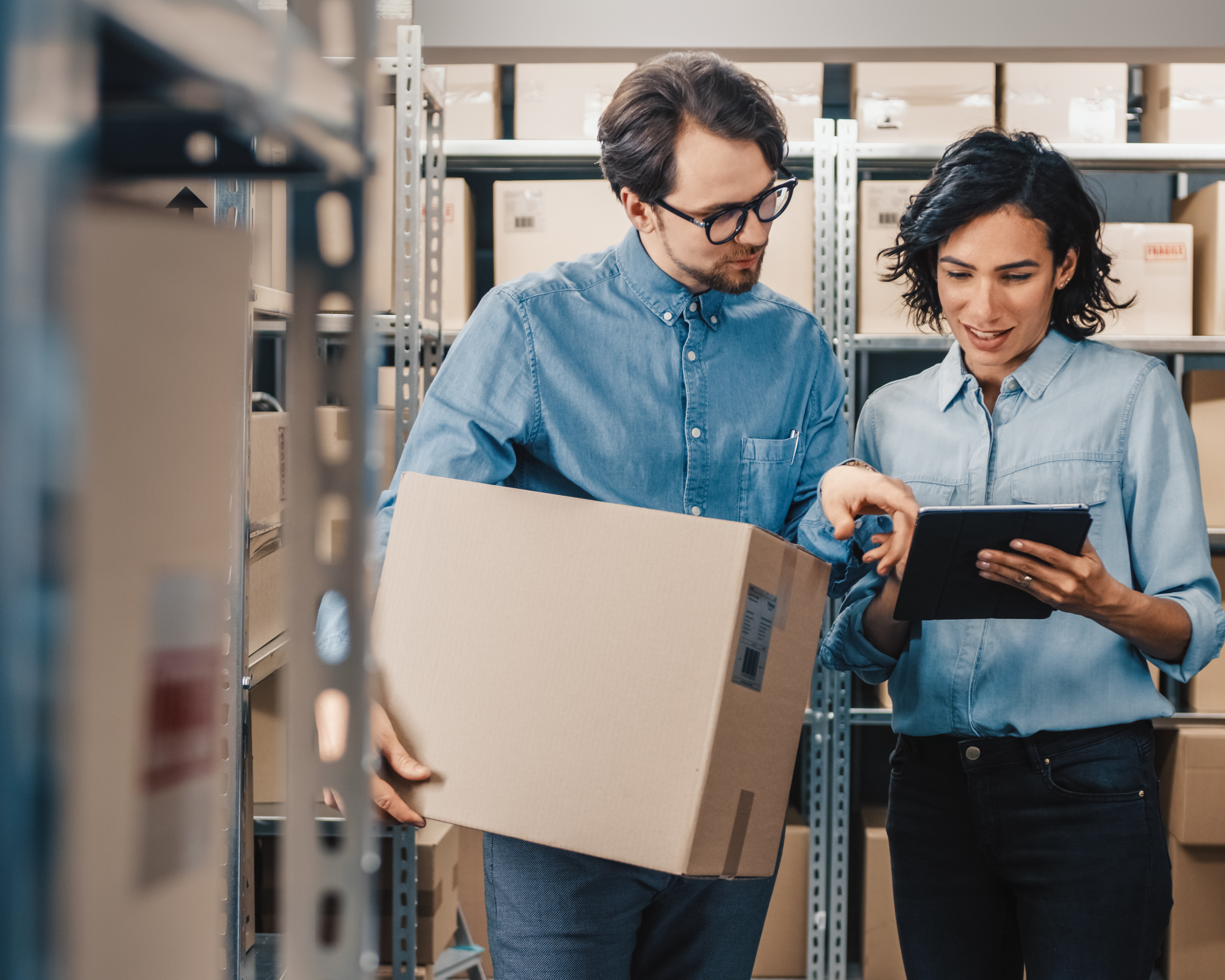 A man holding a box while a woman works on a tablet to schedule delivery
